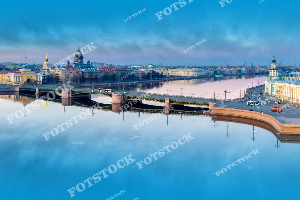 Фотография панорамного вида Санкт-Петербург, Россия, снятая с дрона в летний день. На фото изображён Дворцовый мост, разведённый над рекой Нева. Фотоснимок передаёт масштаб архитектуры Санкт-Петербурга, чёткую геометрию моста и простор водной акватории в ясную летнюю погоду. Это изображение подчёркивает традицию разводных мостов и архитектурный облик исторического центра города. Иллюстрация отражает панораму Петербурга как одного из самых узнаваемых городов России.